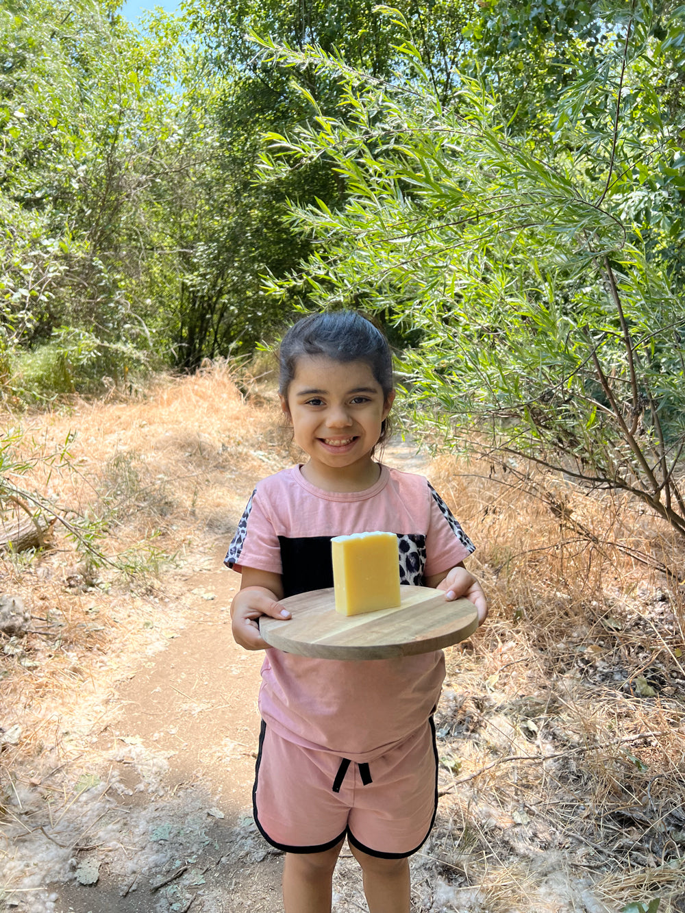 Child holding a wooden board with a bar of soap outdoors